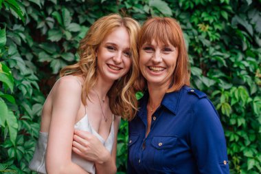 Güzel anne ve yetişkin kızı bir yaz günü yeşil bir arka planda kafa kafaya duruyorlar.