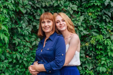 Güzel anne ve yetişkin kızı bir yaz günü yeşil bir arka planda birbirlerine sarılıyorlar.