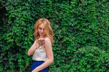 Makyajlı ve kıvırcık sarı saçlı genç bir kadının portresi. Yaban üzüm yapraklarının yanında elinde bir bluz tutuyordu. Boşluğu kopyala.