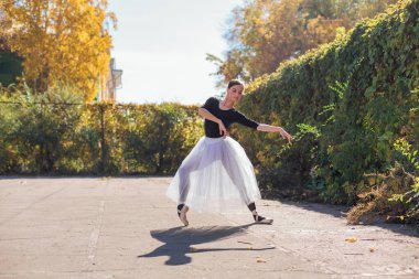 Beyaz etekli kadın balerin altın bir sonbahar parkında sivri ayakkabılarla dans ediyor. Balerin güzel bir bale pozisyonunda duruyor.