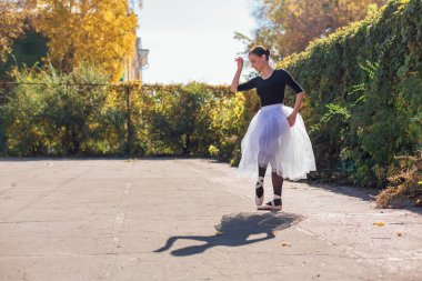 Beyaz etekli kadın balerin altın bir sonbahar parkında sivri ayakkabılarla dans ediyor. Balerin güzel bir bale pozisyonunda duruyor.