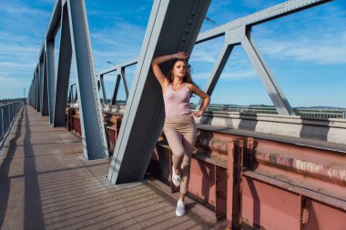 Gün batımında nehrin üzerindeki eski paslı nakliye köprüsünde poz veren genç ve güzel bir kadının ılık yaz portresi..