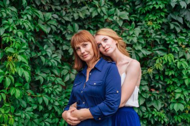 Güzel anne ve yetişkin kızı bir yaz günü yeşil bir arka planda birbirlerine sarılıyorlar.