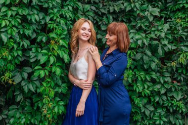 Güzel anne ve yetişkin kızı bir yaz günü yeşil bir arka planda birbirlerine sarılıyorlar.