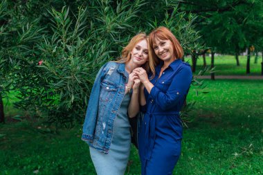 Güzel anne ve yetişkin kızı bir yaz günü yeşil bir arka planda birbirlerine sarılıyorlar.