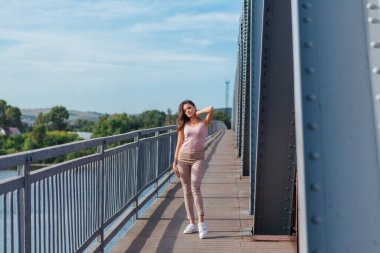 Gün batımında nehrin üzerindeki eski paslı nakliye köprüsünde poz veren genç ve güzel bir kadının ılık yaz portresi..