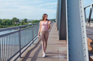 Gün batımında nehrin üzerindeki eski paslı nakliye köprüsünde poz veren genç ve güzel bir kadının ılık yaz portresi..