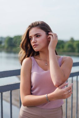 Gün batımında nehrin üzerindeki eski paslı nakliye köprüsünde poz veren genç ve güzel bir kadının ılık yaz portresini kapatın..