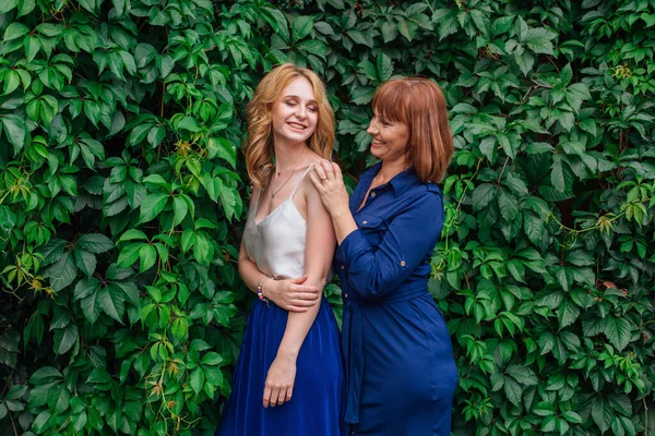 Güzel anne ve yetişkin kızı bir yaz günü yeşil bir arka planda birbirlerine sarılıyorlar.