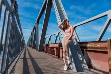 Gün batımında nehrin üzerindeki eski paslı nakliye köprüsünde poz veren genç ve güzel bir kadının ılık yaz portresi..