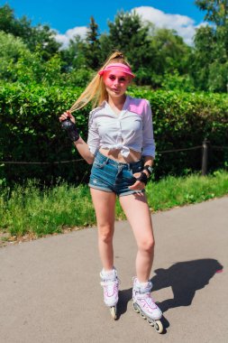 Pembe bir kapak Visor ve paten için koruyucu eldivenler ve yolda paten üzerinde kaykay sürme duygusal güzel bir genç kız portresi.