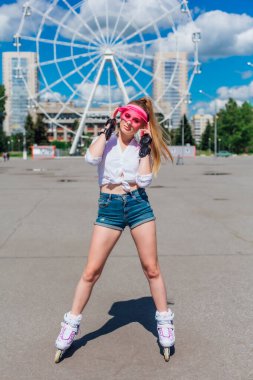 Pembe bir kapak Visor ve paten için koruyucu eldivenler ve yolda paten üzerinde kaykay sürme duygusal güzel bir genç kız portresi.