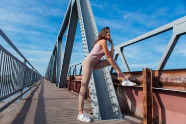 Gün batımında nehrin üzerindeki eski paslı nakliye köprüsünde poz veren genç ve güzel bir kadının ılık yaz portresi..
