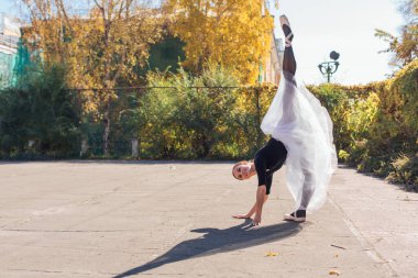 Beyaz etekli kadın balerin altın bir sonbahar parkında sivri ayakkabılarla dans ediyor. Balerin güzel bir bale pozisyonunda duruyor.