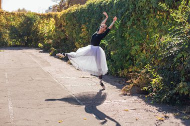 Beyaz etekli kadın balerin altın bir sonbahar parkında sivri ayakkabılarla dans ediyor. Balerin güzel bir bale pozisyonunda duruyor.