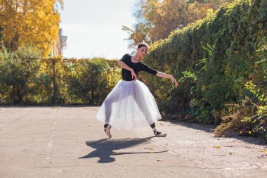 Beyaz etekli kadın balerin altın bir sonbahar parkında sivri ayakkabılarla dans ediyor. Balerin güzel bir bale pozisyonunda duruyor.