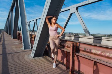 Gün batımında nehrin üzerindeki eski paslı nakliye köprüsünde poz veren genç ve güzel bir kadının ılık yaz portresi..