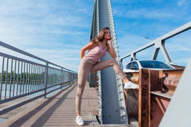 Gün batımında nehrin üzerindeki eski paslı nakliye köprüsünde poz veren genç ve güzel bir kadının ılık yaz portresi..