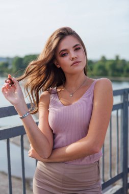 Gün batımında nehrin üzerindeki eski paslı nakliye köprüsünde poz veren genç ve güzel bir kadının ılık yaz portresini kapatın..