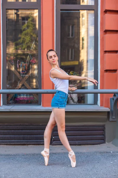 Jeune ballerine en chemise blanche et jeans en short dansant en pointes sur une rue . — Photo