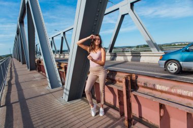 Gün batımında nehrin üzerindeki eski paslı nakliye köprüsünde poz veren genç ve güzel bir kadının ılık yaz portresi..