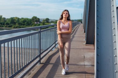 Gün batımında nehrin üzerindeki eski paslı nakliye köprüsünde poz veren genç ve güzel bir kadının ılık yaz portresi..