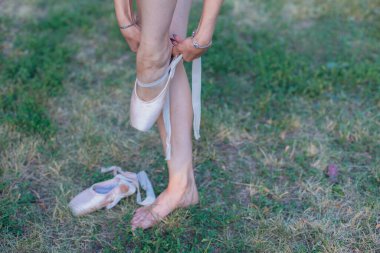 Balerin çimlerin üzerinde duruyor ve bacaklarına noktalar takıyor..