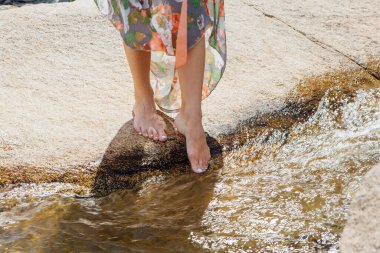 Çıplak ayaklı bir kadın temiz suyla akan nehrin yanında duruyor. Ayağını suya sokacak.