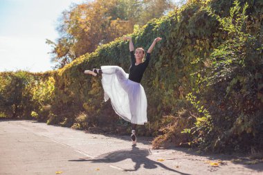 Beyaz etekli kadın balerin altın bir sonbahar parkında sivri ayakkabılarla dans ediyor. Balerin güzel bir bale pozisyonunda duruyor.