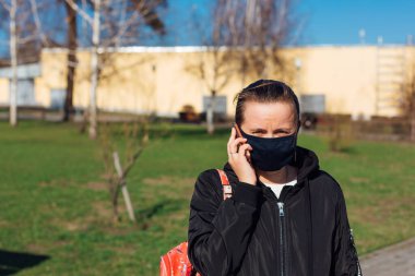 Elinde cep telefonu tutan siyah kumaş maskeli beyaz bir kadın. Coronavirus COVID-19 gibi mikropların yayılmasını önlemek için tıbbi maske kullanma kavramı.