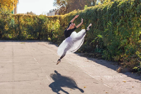 Beyaz etekli kadın balerin altın bir sonbahar parkında sivri ayakkabılarla dans ediyor. Balerin atlayışı yapıyor.