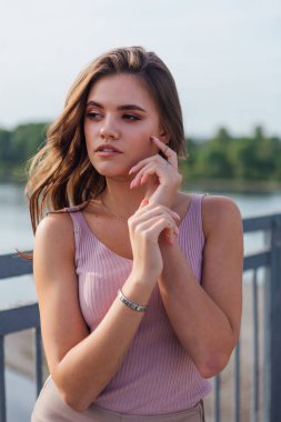 Gün batımında nehrin üzerindeki eski paslı nakliye köprüsünde poz veren genç ve güzel bir kadının ılık yaz portresini kapatın..