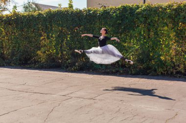 Beyaz etekli kadın balerin altın bir sonbahar parkında sivri ayakkabılarla dans ediyor. Balerin atlayışı yapıyor.