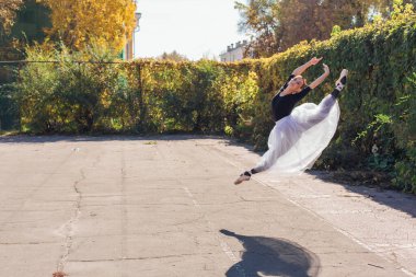 Beyaz etekli kadın balerin altın bir sonbahar parkında sivri ayakkabılarla dans ediyor. Balerin atlayışı yapıyor.