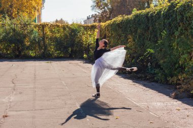 Beyaz etekli kadın balerin altın bir sonbahar parkında sivri ayakkabılarla dans ediyor. Balerin güzel bir bale pozisyonunda duruyor.