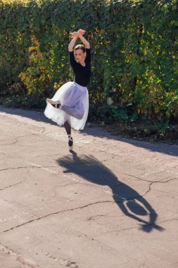 Beyaz etekli kadın balerin altın bir sonbahar parkında sivri ayakkabılarla dans ediyor. Balerin güzel bir bale pozisyonunda duruyor.