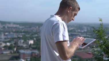 Adam dışarıda tablet üzerinde çalışıyor, işinden memnun.