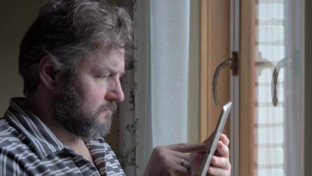 Hombre de negocios bebiendo café y trabajando en una tableta junto a la ventana, está satisfecho con su trabajo — Vídeos de Stock