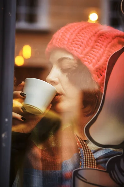 Woman by the window in a pink hat . She is drinking coffee — 图库照片