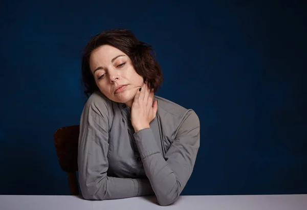 Young worried woman. She sits at a table against on a dark blue background — Stock Photo, Image