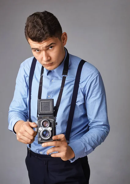 Een man met een oude camera in de studio. Guy schiet op een oude vintage film camera met twee lenzen. — Stockfoto