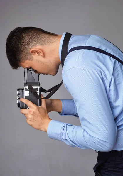 Een man met een oude camera in de studio. Guy schiet op een oude vintage film camera met twee lenzen. — Stockfoto