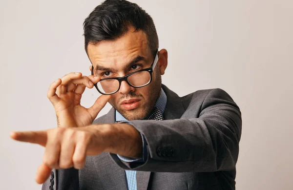 Un joven empresario mira algo desde debajo de sus gafas y señala con el dedo —  Fotos de Stock