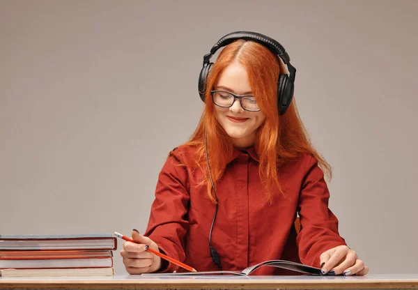 Kızıl saçlı, kulaklıklı kız öğrenci öğreniyor. — Stok fotoğraf
