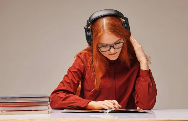 Rödhårig kvinnlig student i hörlurar hon lär sig — Stockfoto