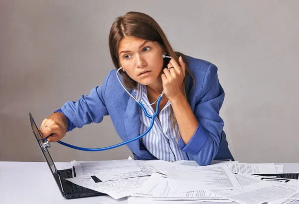 Trabalhadora olha e ouve seu laptop com um fonendoscópio — Fotografia de Stock