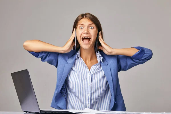 Una mujer de negocios enojada en el lugar de trabajo, hablando en dos teléfonos inteligentes a la vez — Foto de Stock