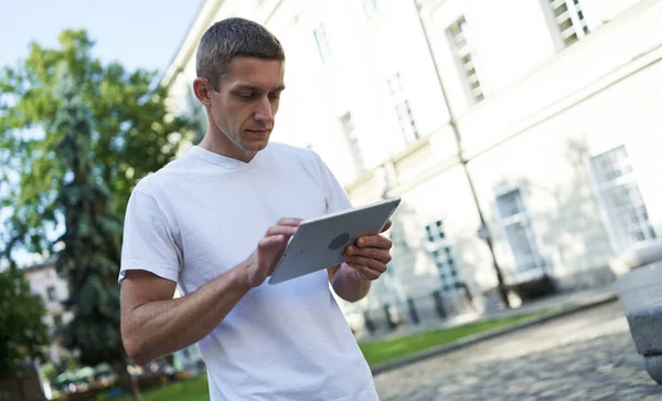 Pohledný muž stojící na ulici a hledající něco na svém tabletu — Stock fotografie