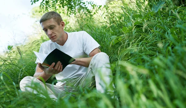 Hombre sentado en la tranquila hierba verde y leyendo un libro —  Fotos de Stock