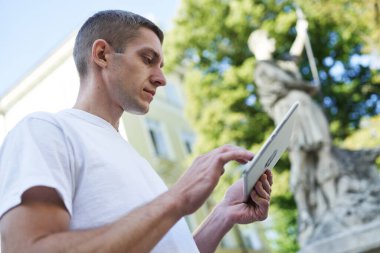 Sokakta duran yakışıklı genç adam tabletinde bir şey arıyor.